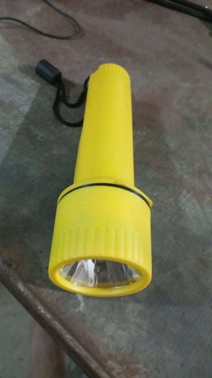 A yellow plastic torch with a black wrist strap lies on a dark, textured surface.