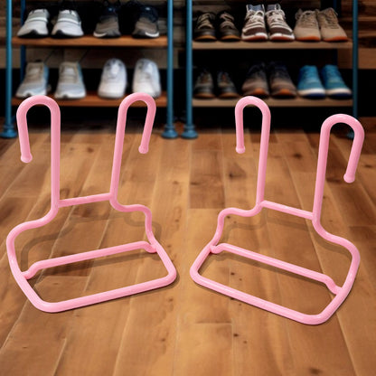 Two pink plastic shoe drying racks rest on a wooden floor in front of a shoe rack filled with various footwear.