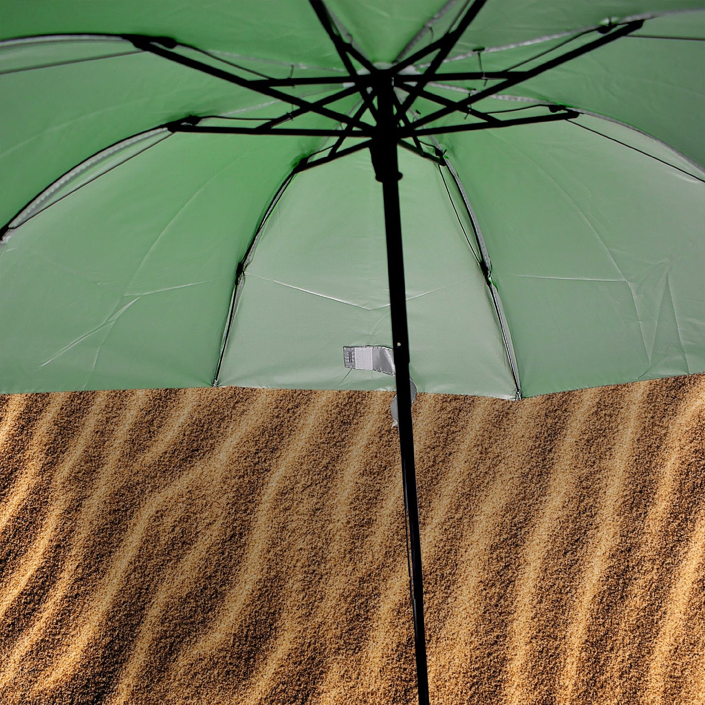 The underside of an open green umbrella reveals its black frame and silver lining, above a textured brown surface.