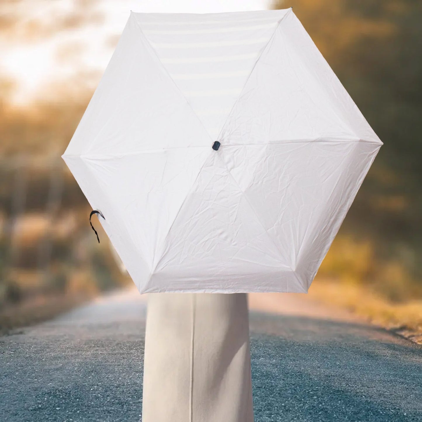 A white hexagonal umbrella is open, held by an unseen person, against a blurred road background.