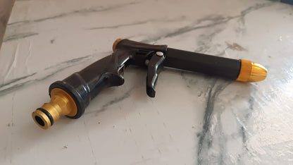 Brass water spray gun attached to a hose, powerfully spraying water during outdoor cleaning.