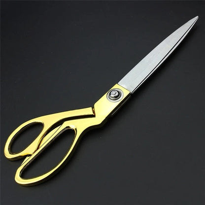 Top-down view of golden tailoring scissors with sharp stainless steel blades on a flat surface.