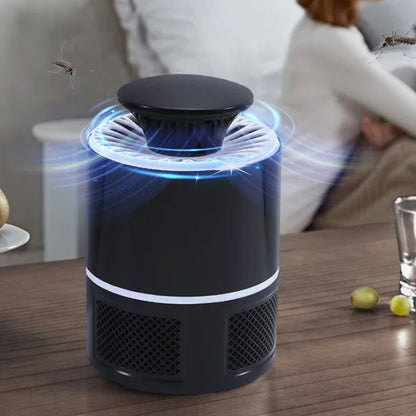 A black Mosquito Killer Lamp with blue light and swirling effects, on a table with a person in the background.