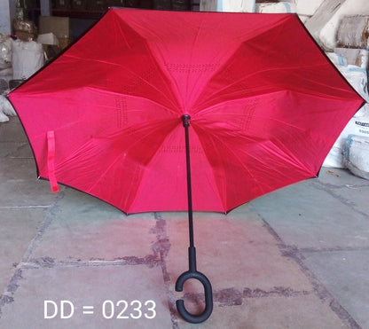 An open, bright red reverse umbrella with a C-shaped handle is displayed on a concrete floor in a warehouse setting.