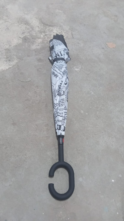 A closed reverse umbrella with a black and white newspaper print is standing upright on a grey concrete surface.