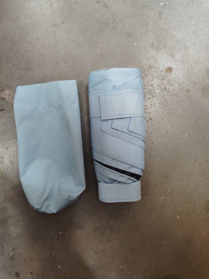 A light blue folded umbrella with a matching storage pouch lies on a concrete surface.